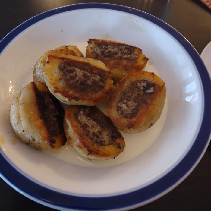 Halverade, stekta kroppkakor på en vit tallrik med blå kant.