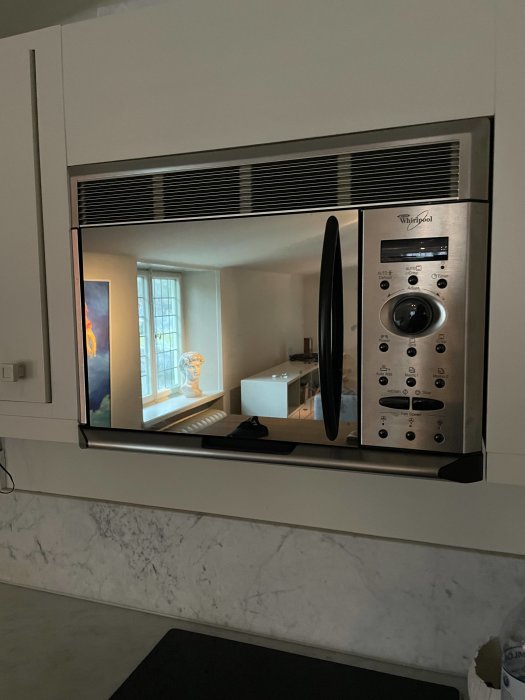 Inbyggd mikrovågsugn från Whirlpool monterad över marmorliknande köksbänk med spegling av rummet.