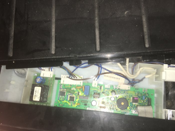 Öppen elektronisk enhet med synligt kretskort och kopplingskablar mot en svart bakgrund.