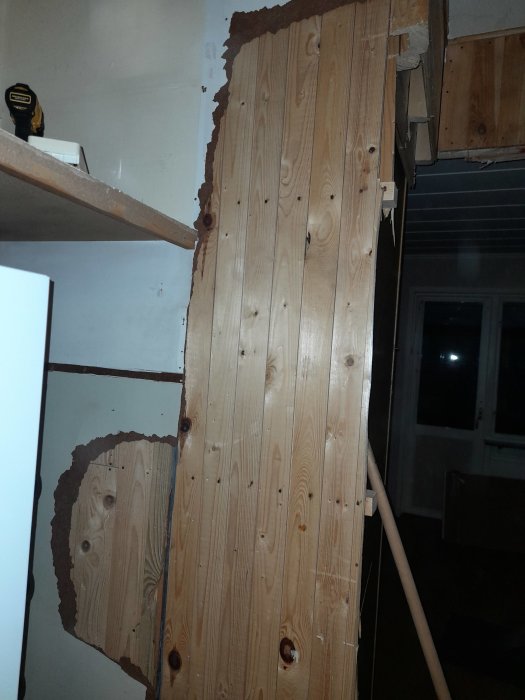En vägg under rivning med exponerade träreglar och delvis borttagen väggpanel.