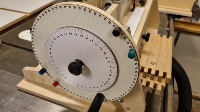 Justerverktyg med skala för fininställning vid 1mm delningar, framför träbit med fingerskarvningar.