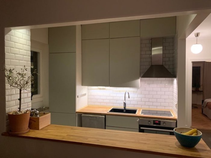 Renoverat kök med nymålade gröna luckor, träbänkskiva, vita väggkakel och inbyggda vitvaror.