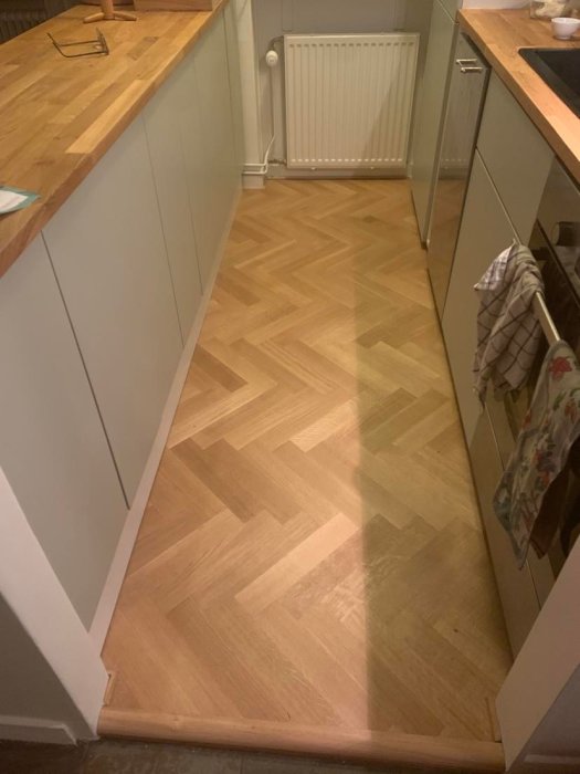 Renoverat kök med nymålade gröna skåpluckor och träarbetsbänk, samt fiskbensparkettgolv.