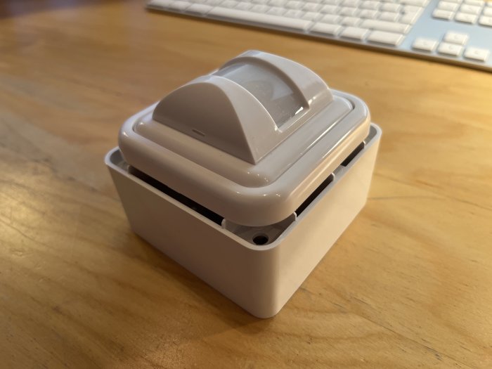 En rörelsevakt med vit ram som ser ut att inte passa perfekt, placerad på ett bord med tangentbord i bakgrunden.