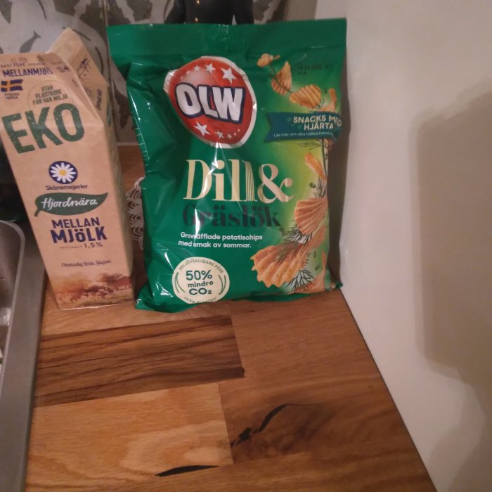 Förpackning av OLW dill och gräslök potatischips samt en mjölkförpackning på ett köksbord.