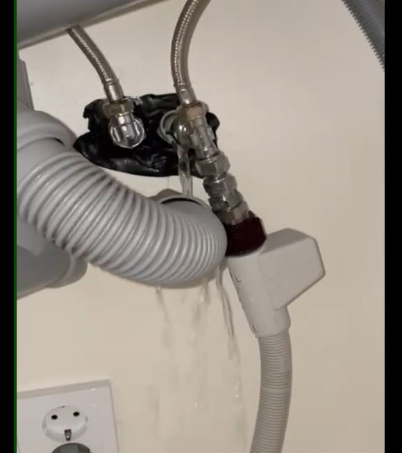 Vattenläcka under diskhon med vatten som forsar från rörkopplingar.