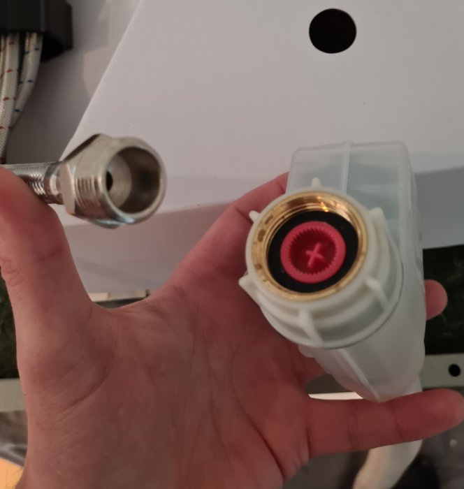 Hand håller en diskmaskinsanslutning med metallkoppling och röd tätning.