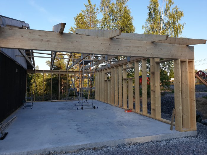 Konstruktion av garage med isolerade träväggar och limträbalk ovanför en betongplatta, byggställningar syns.