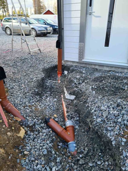 Avloppsinstallation utomhus med rör och grus kring byggnad under konstruktion.