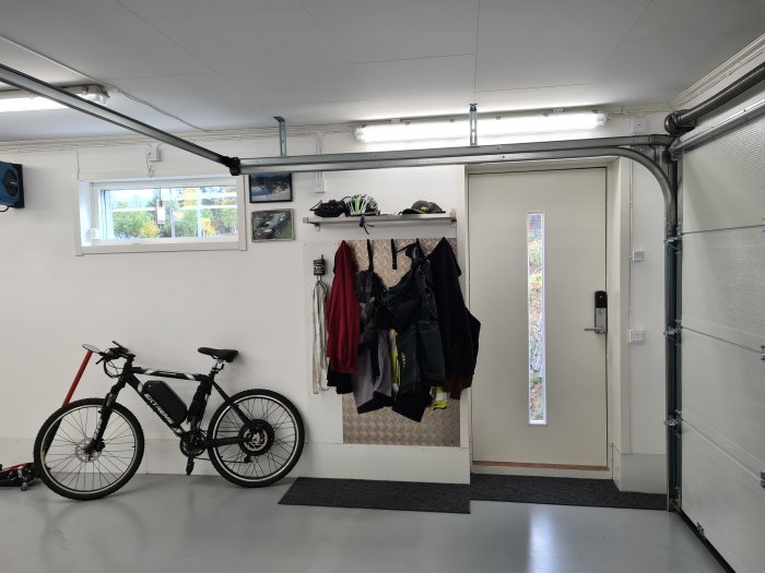 En välorganiserad garageinteriör med cykel, hyllor med kläder, en dörr, ett fönster och LED-belysning under taket.