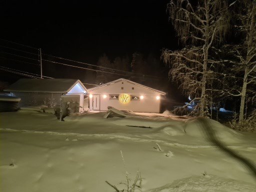 Garage med upplyst fasad och egentillverkad WW-skylt i ett snötäckt nordiskt landskap nattetid.