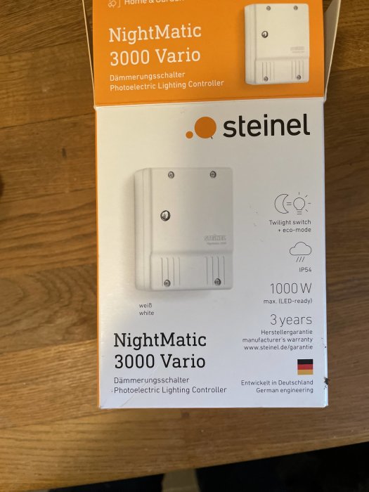 Steinel NightMatic 3000 Vario skymningsrelä i vit färg ligger på en yta bredvid sin förpackning.