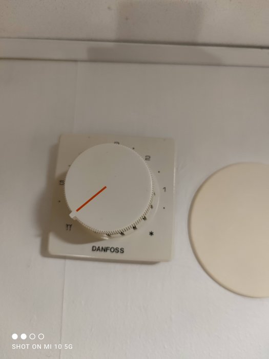 Termostat med numrerad skala och reglage märkt "Danfoss", monterad på vit vägg.