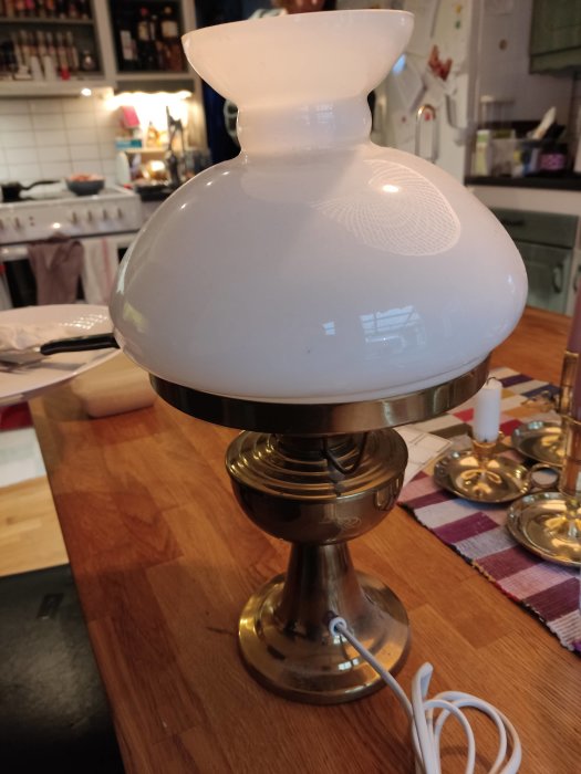 Arvegods lampa med vit skärm och mässingfot på ett köksbord, ojordad med synlig sladd.