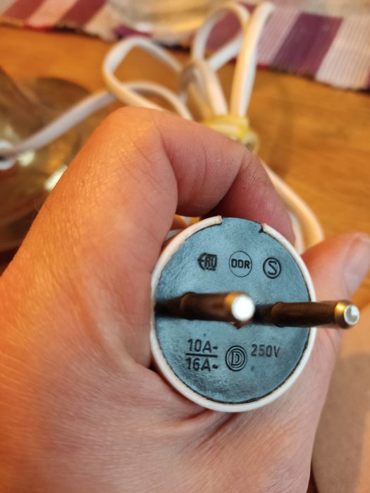 Närbild på en hand som håller en ojordad lampkontakt med två poler.