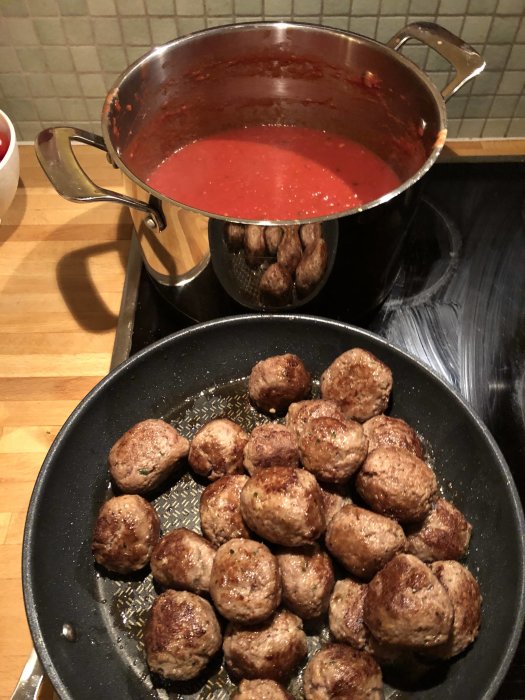 Stekta italienska köttbullar i stekpanna bredvid en kastrull med tomatsås.