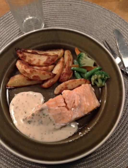 Tallrik med ugnsbakad lax, potatisklyftor, grönsaker och vitvinssås.