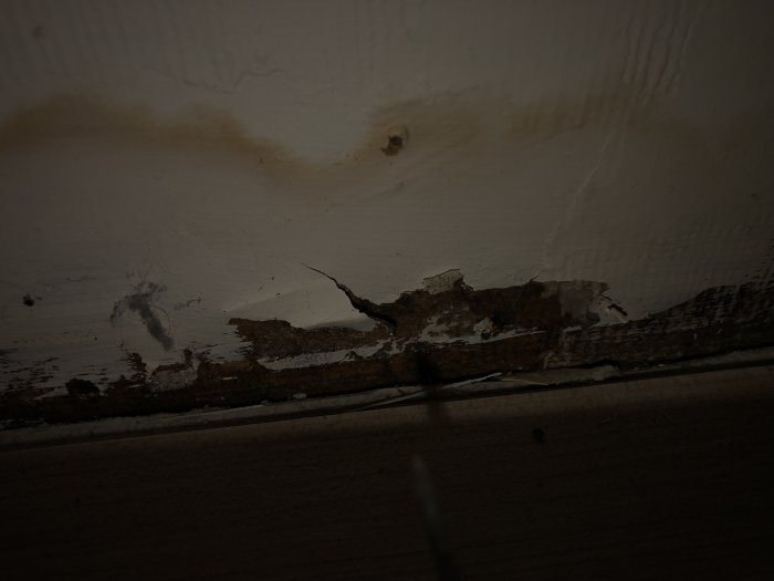 Vägg med fuktskador och avlägsnad golvlist under ett fönster.