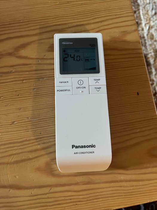 Panasonic luftkonditionerings fjärrkontroll med inställd temperatur på 24 grader Celsius på ett träbord.