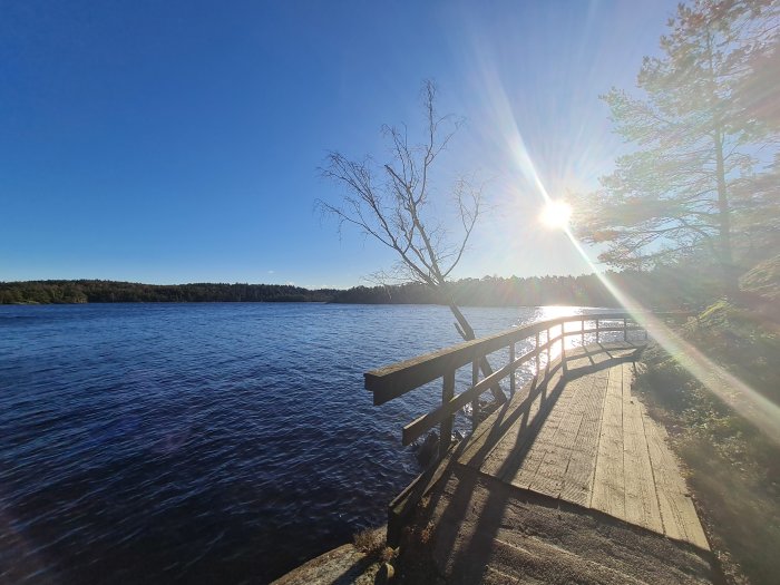 Tranquilt landskap med solstrålar över en sjö och skadad träbrygga efter stormen Malik.