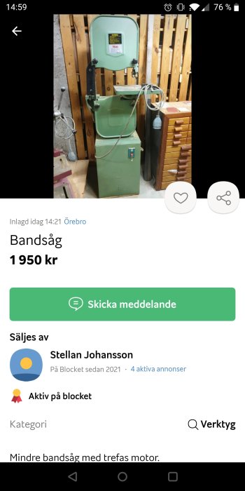 Grön och grå bandsåg i ett verkstadsutrymme med trälådor och verktyg i bakgrunden.