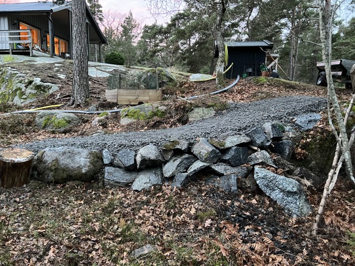 Nybyggd grusväg på ojämn tomt med stora stenar och grönska i bakgrunden.