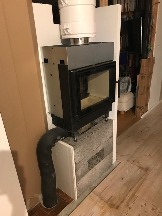 Renoveringsprojekt med en nyinstallerad kamin, omgiven av vit inkapsling och friskluftskanal, före färdigställande.