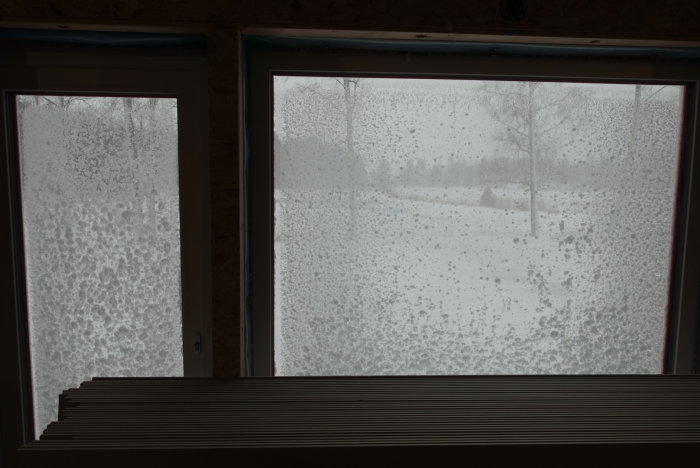 Utsikt från ett fönster i ett bygge med snötäckta rutor och suddig natur i bakgrunden.