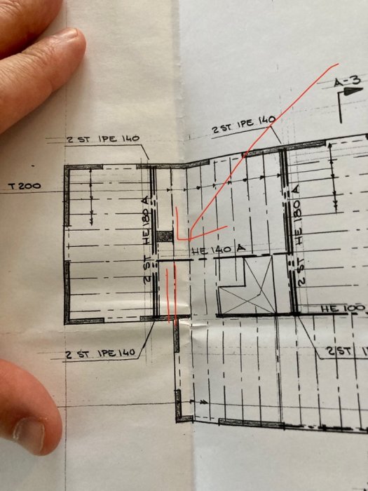 Hand håller arkitektritning med röd markering av valv som ska rivas och dimensioner för stålbalkar.