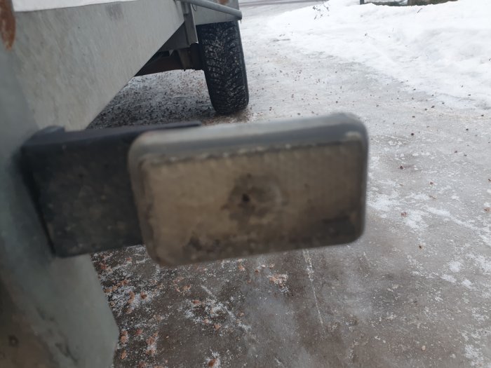 Närbild på ett smutsigt reflex-/positionsljus på ett fordon med snöig mark i bakgrunden.