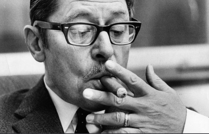 Svartvit bild av en man i kostym som funderar och röker en cigarett.
