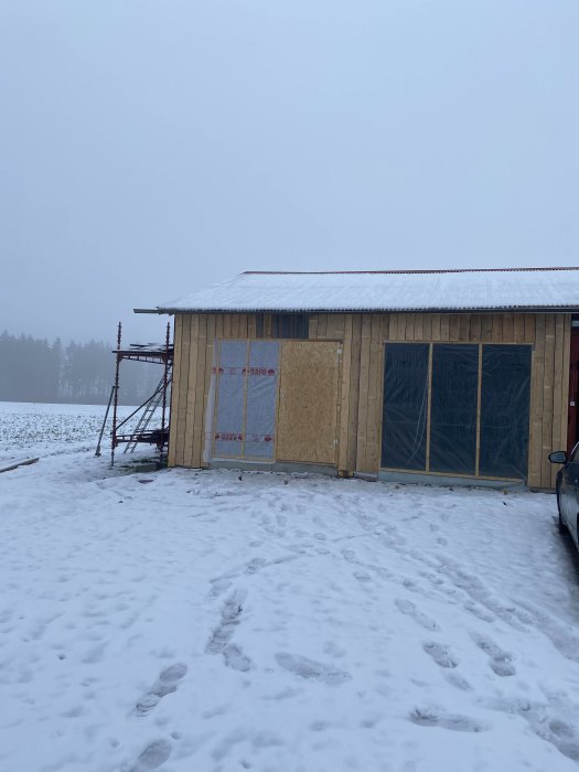 Ny bondsågad panel på byggnad under uppbyggnad med vindduk och temporära dörrar i vintermiljö.