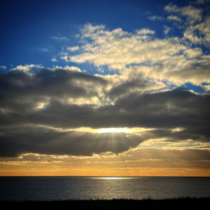 Solstrålar som bryter genom molnen över havet vid solnedgången.