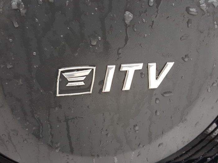 Närbild på en våt bil med logotypen "EITV" i silverfärgat metall mot svart bakgrund.