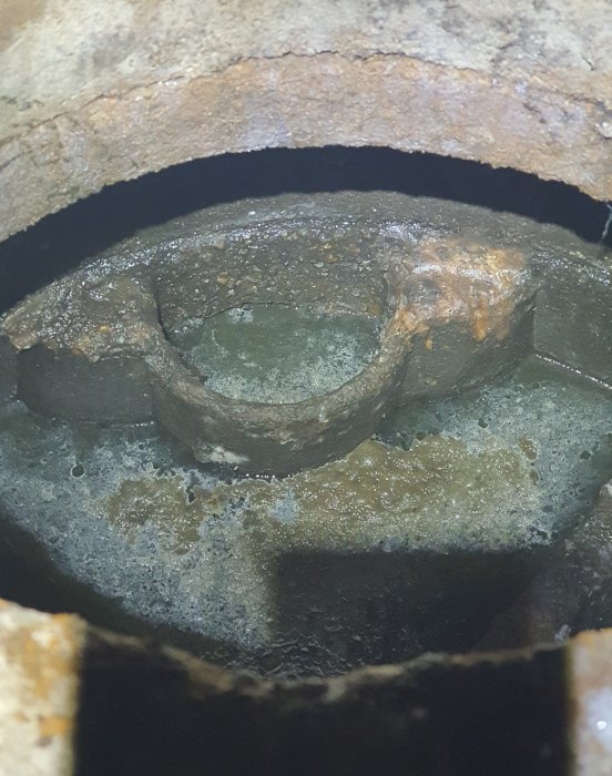 Utsnitt av ett utflödesrör med en krag-liknande formation i ett schakt fyllt med vatten.