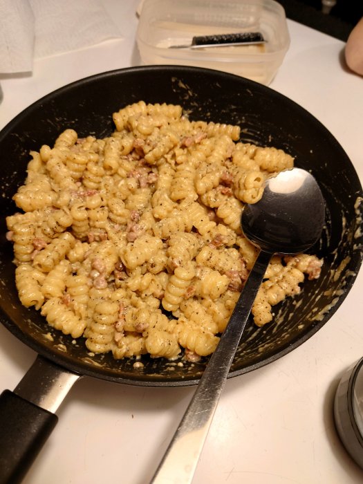 Pasta med pecorino och tärnad pancetta i stekpanna, redo att serveras.