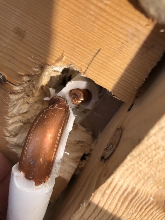 Avsnitt av kopparrör synligt genom borrat hål i regel, omgivet av skalade plastdelar.