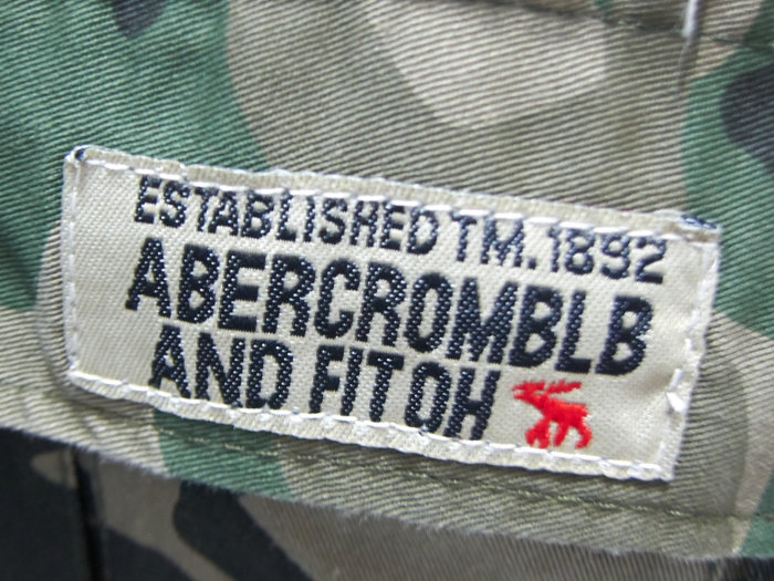 Felstavad logga på klädtextil: "ESTABLISHED TM. 1892 ABERCROMBLB AND FITOH" med en röd älgfigur.