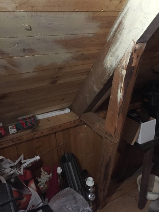 Snedtak och vägg på en kattvind med synliga träbjälkar och förrådsföremål, behov av isolering.