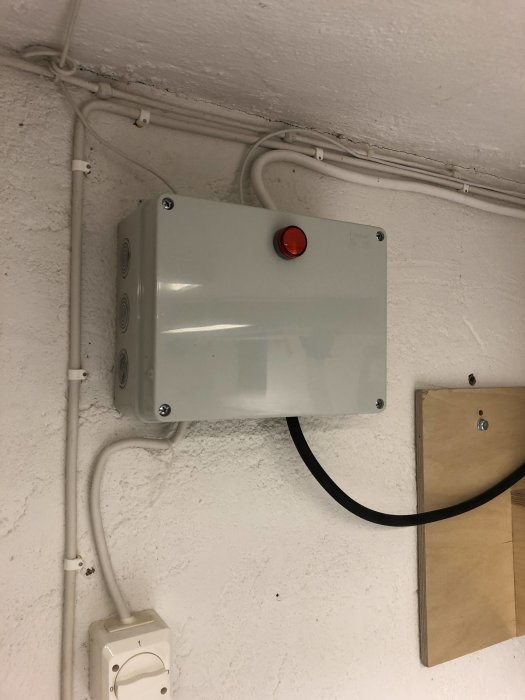 Elektriskt styrskåp med röd indikatorlampa installerat på en vit vägg med kablar och ledningar.