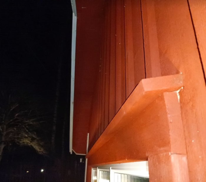 Rödmålad husvägg with takutsprånget och ventilen under, nattbild som visar fönster och fukt på fönsterkarmens hörn.