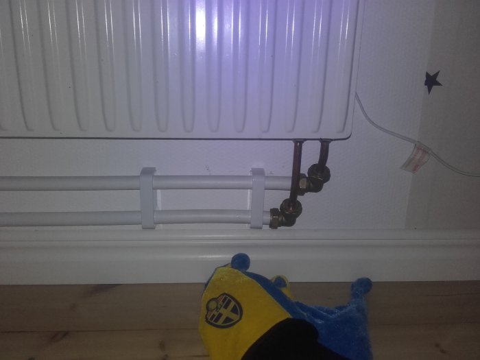 Installation av rör vid en radiator, synlig lutning, med en leksak framför.