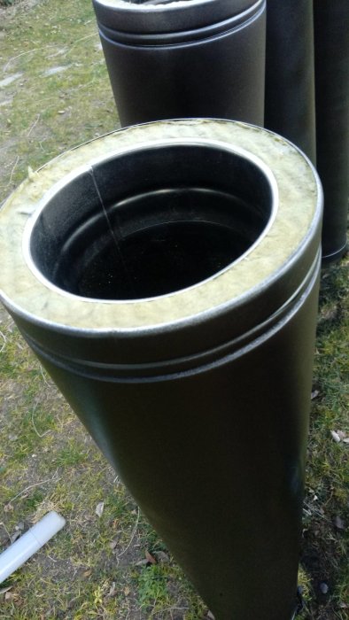 Ett staplat set med stora gröna plastbehållare för bygg- eller trädgårdsavfall syns på gräs.