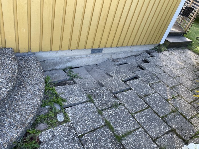 Erosion vid husgrund och skadade stenplattor efter översvämning.