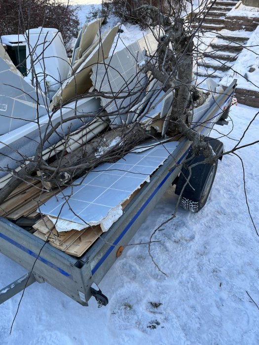 Avsliten äppelträdsgren ligger på en släpvagn fylld med byggavfall i vintersnö.