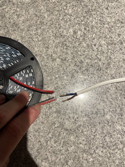LED-slinga med avskalade ändar bredvid ett eluttagskabel på granitbänk.