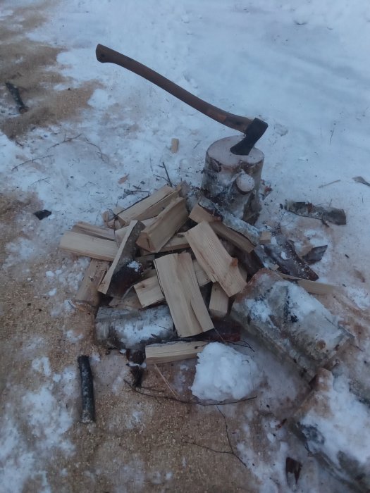 Klyvd björkved och yxa på stubbe i vintersnö.