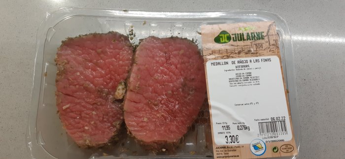 Två råa kalvmedaljonger i förpackning bredvid etikett med produktinformation.