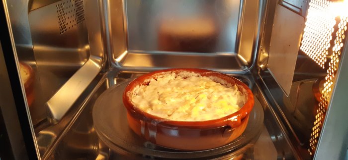 Potatisgratäng som tillagas i mikrovågsugn, ångor syns och gratängen ser gräddig ut.