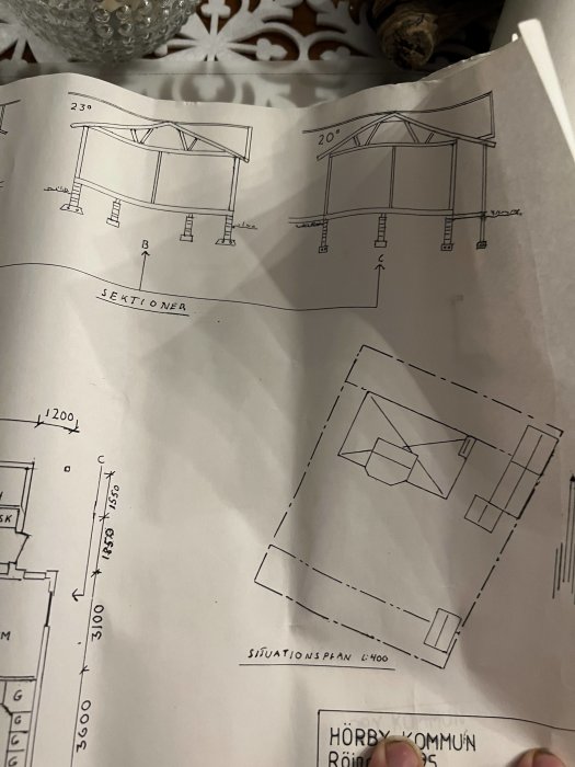 Handritade arkitekturritningar med sektionsvyer och situationsplan för ett byggprojekt.